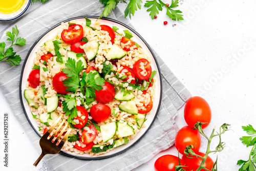 Bulgur tabbouleh salad with tomatoes, cucumbers and parsley. Traditional Middle Eastern dish. White table background, top view
