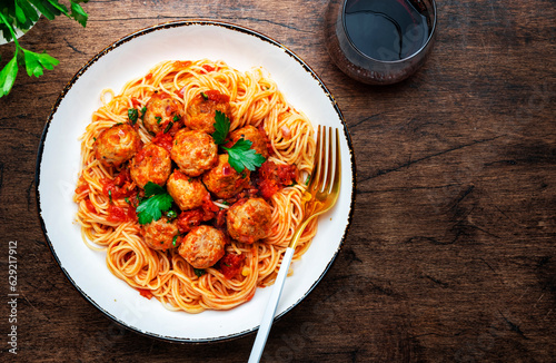 Spaghetti pasta with pork and beef meatballs in tomato sauce with parsley in plate, wooden table background, top view