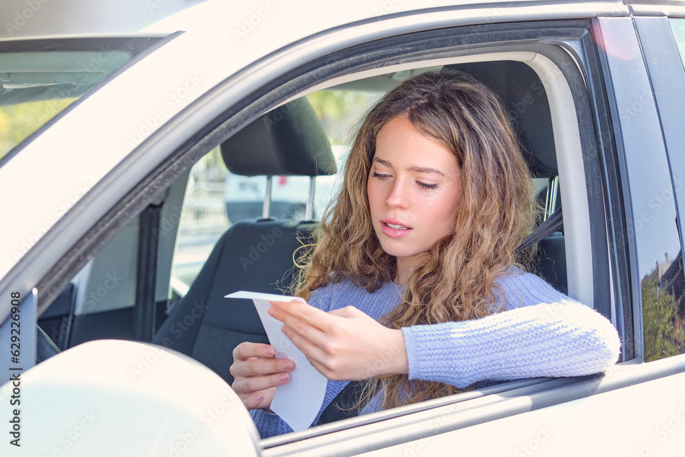 Young woman reading penalty receipt in car drivers seat