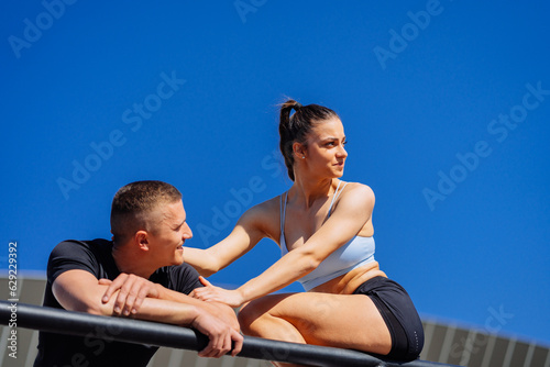 Sexy sporty girl sitting on a fence and looking somewhere while her boyfriend is talking and looking at her