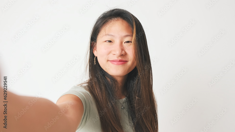 Smiling girl in gray top takes selfie , makes video call on white background, studio shot Smiling girl in gray top takes selfie , makes video call on white background, studio shot