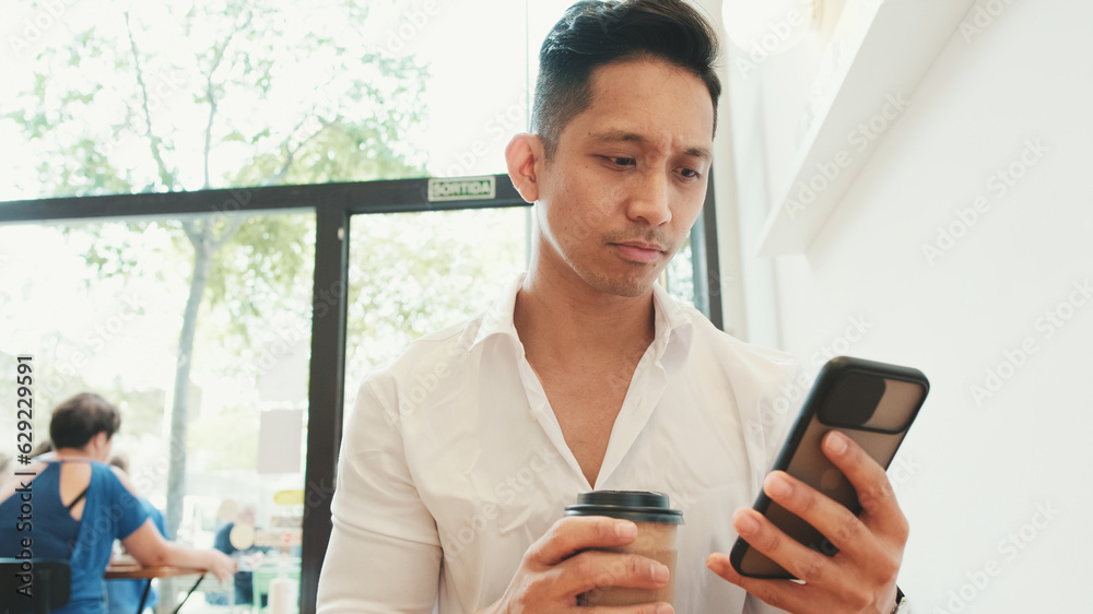 Young businessman sits at table with mobile phone and drinks coffee in cafe Young businessman sits at table with mobile phone and drinks coffee in cafe