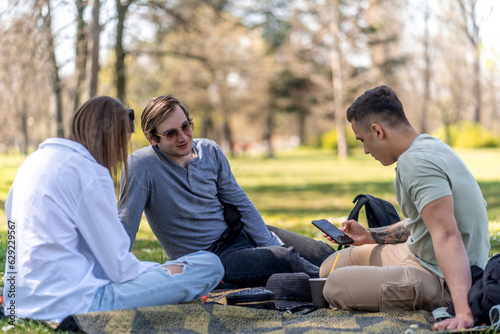Shot of young man and two woman sitting together outdoors on grass field