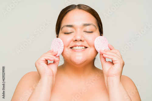 Excited fat woman exfoliating her skin with sponges photo