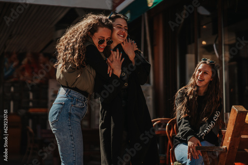 Two girls having beautiful conversation and hugging. Their female brunette friend is looking at them and smiling