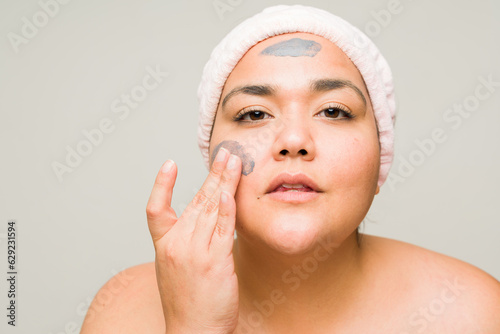 Beautiful big woman using skin care products and mud mask