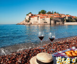 Two glasses with red wine and croissants on the beach in Budva against the backdrop of the island of Sveti Stefan