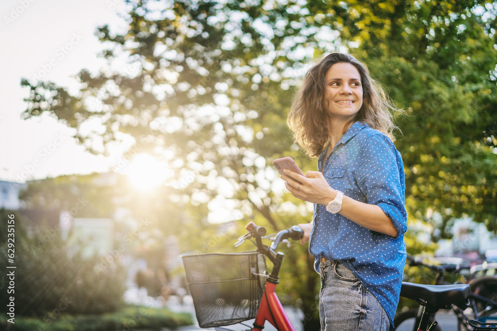 A young Caucasian woman using a phone while standing next to her bicycle in the city street.