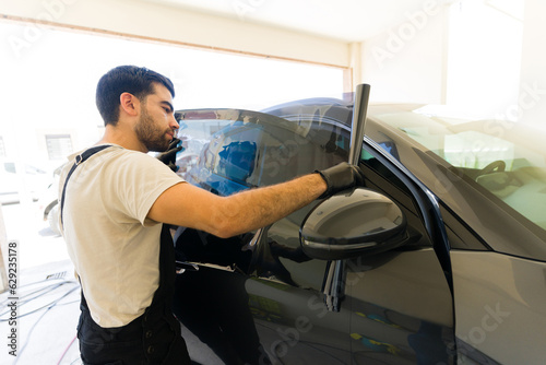 Specialist installing car tint on vehicle window at workshop