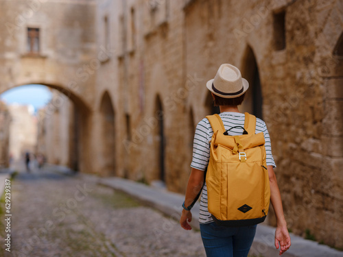 summer trip to Rhodes island Greece. Young Asian woman in striped tshirt and hat walks Street of Knights of Fortifications castle. female traveler visiting southern Europe. Unesco world heritage site © YURII Seleznov