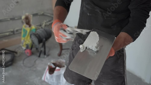 Caucasian professional builder man at work preparing plaster to improve and remodel white surface on indoor drywalls in house construction site, domestic interior. Closeup shot on hands detail