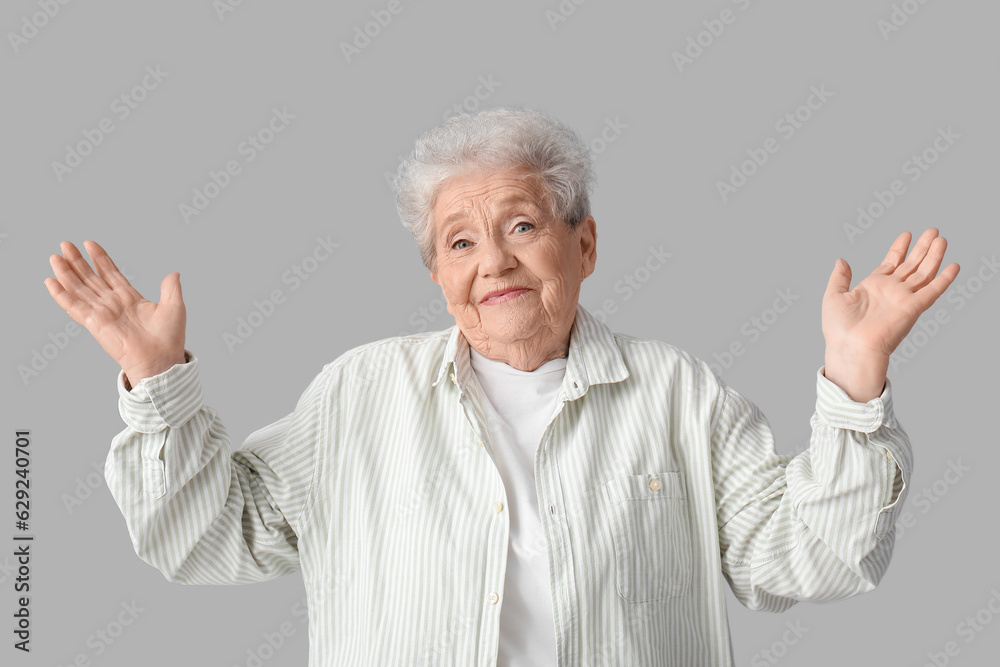 Senior woman shrugging on grey background Senior woman shrugging on grey background
