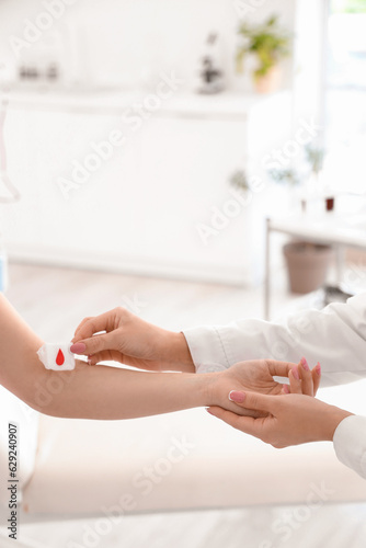 Female doctor applying gauze on donor's arm in clinic, closeup