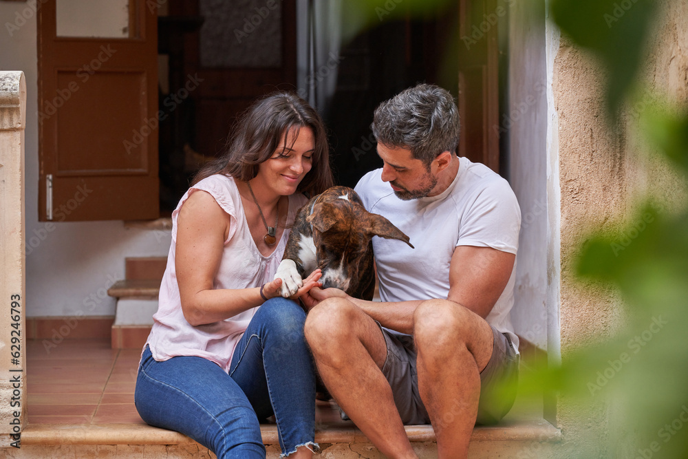 Happy couple caressing dog on porch of house