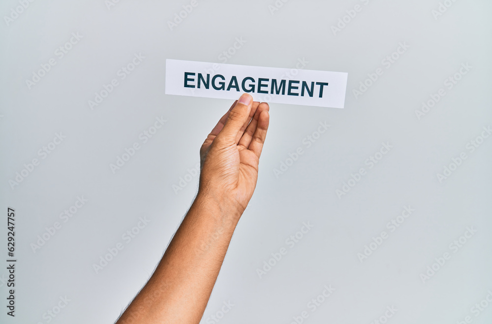 Hand of caucasian man holding paper with engagement word over isolated white background Hand of caucasian man holding paper with engagement word over isolated white background