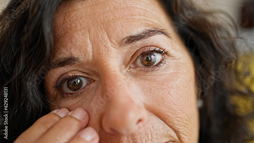 Foto Middle age hispanic woman touching baggy eyes at home