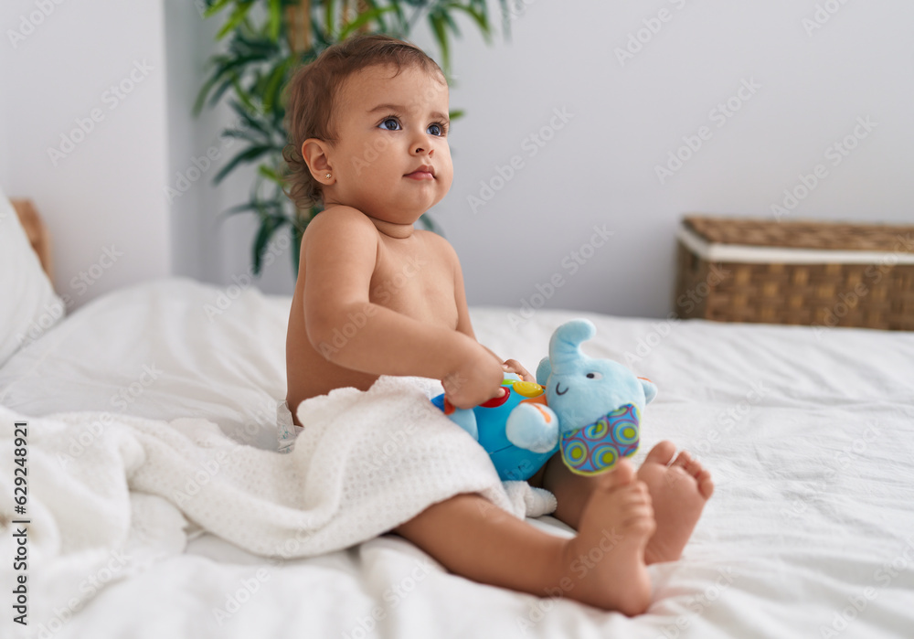 Adorable hispanic baby sitting on bed playing with elephant doll at bedroom Adorable hispanic baby sitting on bed playing with elephant doll at bedroom