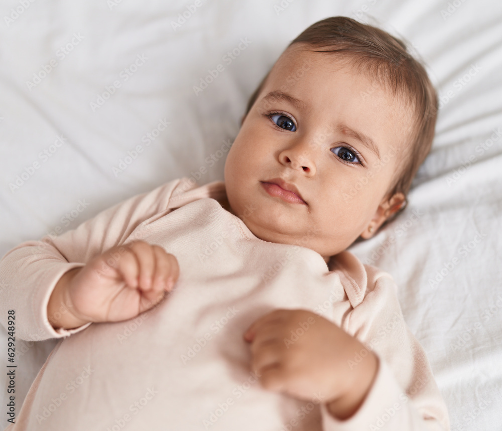 Adorable hispanic baby lying on bed with relaxed expression at bedroom