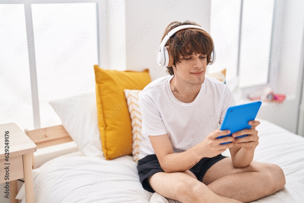 Young blond man watching video on touchpad sitting on bed at bedroom Young blond man watching video on touchpad sitting on bed at bedroom