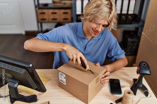 Young blond man ecommerce business worker unpacking cardboard box at office