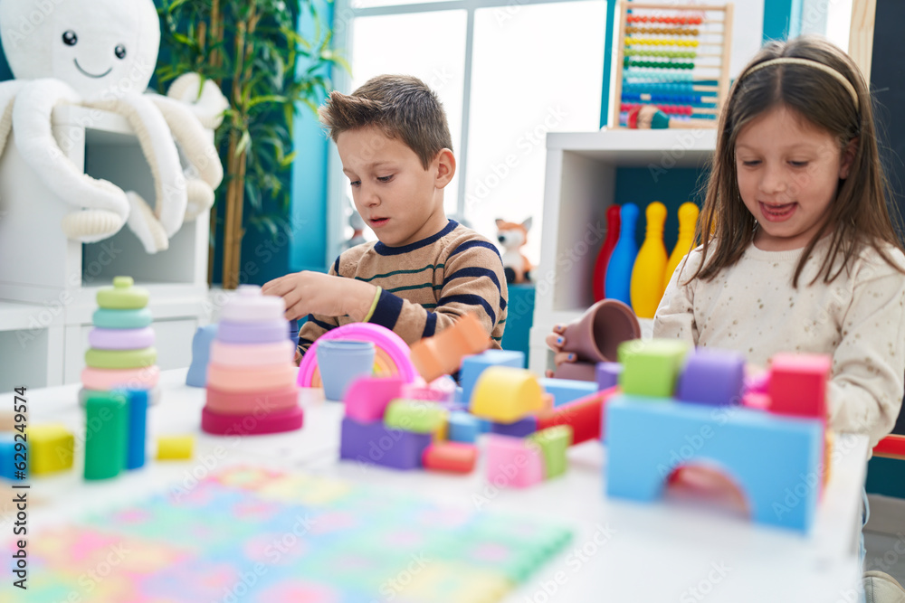 Fototapeta premium Adorable boy and girl playing with construction blocks sitting on table at kindergarten