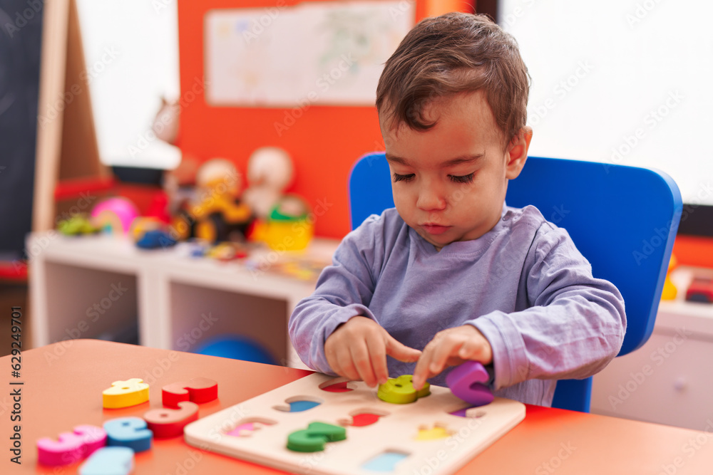 Adorable hispanic boy playing with maths puzzle game sitting on table at kindergarten Adorable hispanic boy playing with maths puzzle game sitting on table at kindergarten