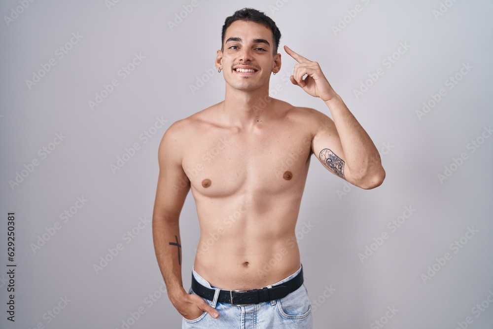 Handsome hispanic man standing shirtless smiling pointing to head with one finger, great idea or thought, good memory