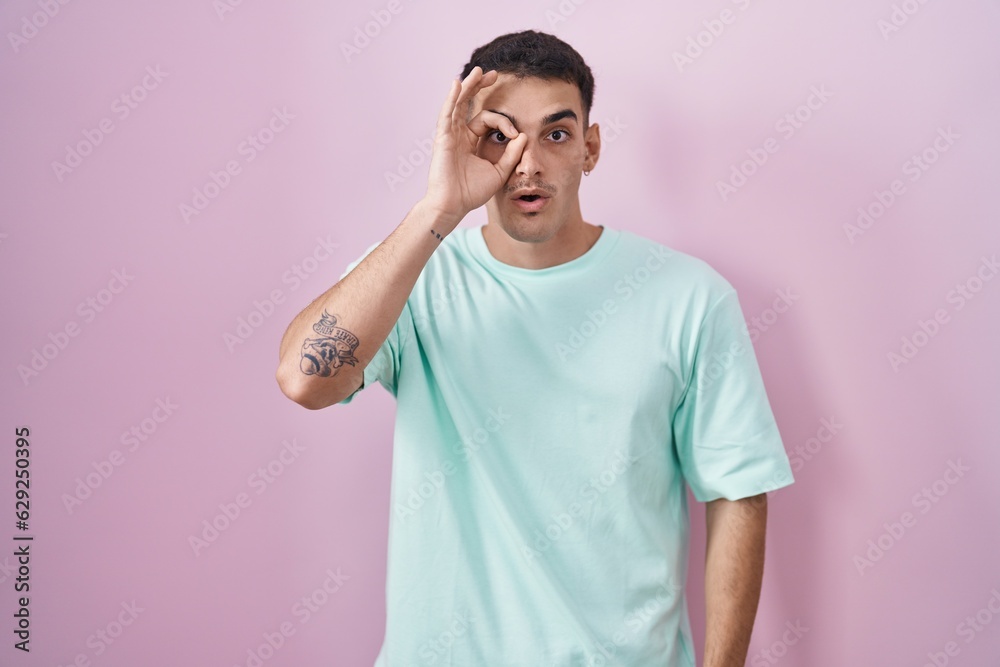 Handsome hispanic man standing over pink background doing ok gesture shocked with surprised face, eye looking through fingers. unbelieving expression. Handsome hispanic man standing over pink background doing ok gesture shocked with surprised face, eye looking through fingers. unbelieving expression.