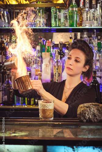 Valokuva Concentrated female barkeeper making flame while mixing cocktail