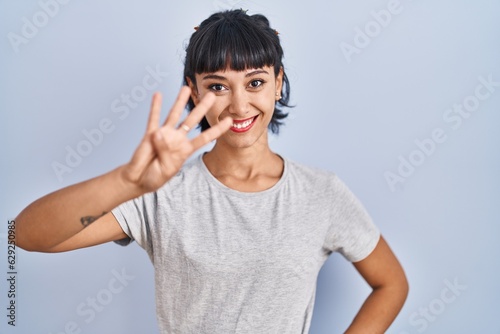 Young hispanic woman wearing casual t shirt over blue background showing and pointing up with fingers number four while smiling confident and happy.