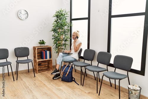 Young blonde woman talking on smartphone writing on document sitting on chair at waiting room © Krakenimages.com