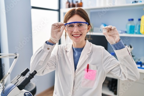 Young blonde woman scientist holding sample smiling at laboratory