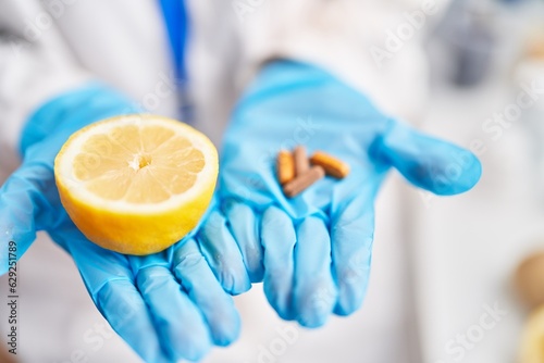 Young blonde woman scientist holding middle lemon and pills at laboratory