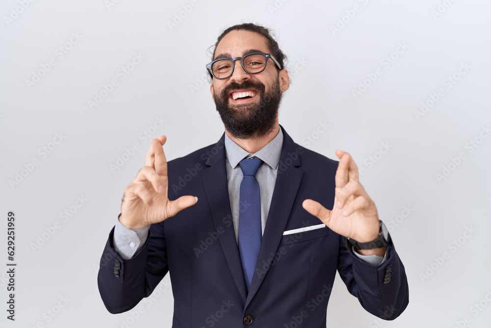 Hispanic man with beard wearing suit and tie gesturing finger crossed smiling with hope and eyes closed. luck and superstitious concept. Hispanic man with beard wearing suit and tie gesturing finger crossed smiling with hope and eyes closed. luck and superstitious concept.