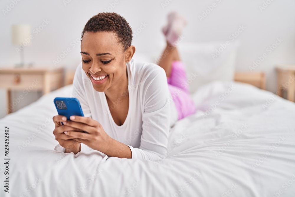 African american woman using smartphone lying on bed at bedroom African american woman using smartphone lying on bed at bedroom