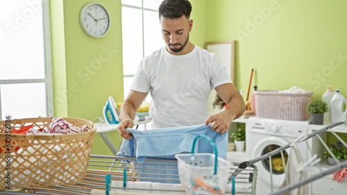 Young arab man hanging clothes on clothesline at laundry room
