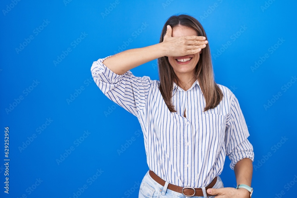 Φωτογραφία Hispanic young woman standing over blue background smiling and laughing with hand on face covering eyes for surprise