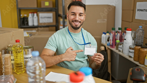 Young arab man volunteer smiling confident pointing to id card at charity center