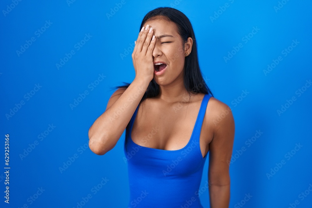 Hispanic woman standing over blue background yawning tired covering half face, eye and mouth with hand. face hurts in pain.