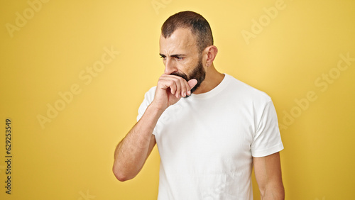 Young hispanic man coughing over isolated yellow background