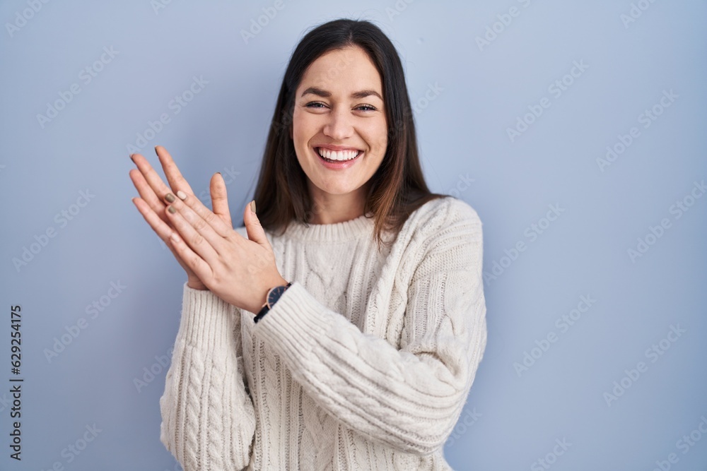 Young brunette woman standing over blue background clapping and applauding happy and joyful, smiling proud hands together Young brunette woman standing over blue background clapping and applauding happy and joyful, smiling proud hands together