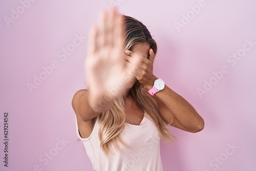 Young blonde woman standing over pink background covering eyes with hands and doing stop gesture with sad and fear expression. embarrassed and negative concept.