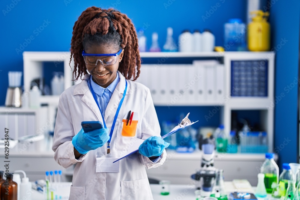 African american woman scientist using smartphone reading document at laboratory