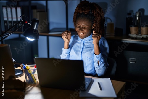 African woman working at the office at night excited for success with arms raised and eyes closed celebrating victory smiling. winner concept.