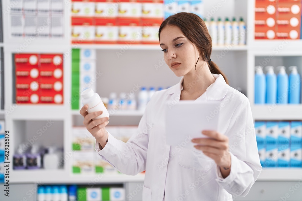 Young woman pharmacist reading prescription holding pills at pharmacy