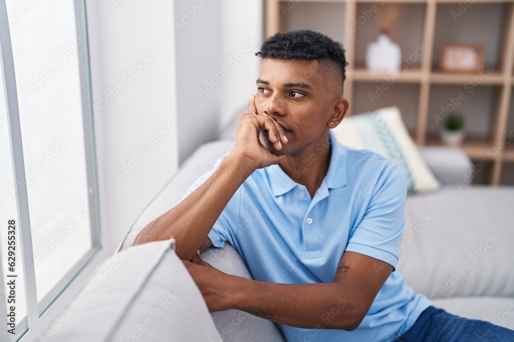 Young latin man looking to the window sitting on sofa at home