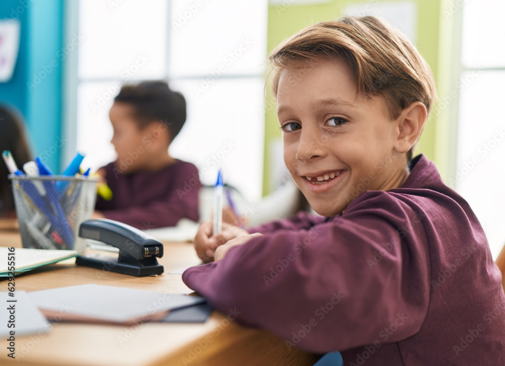 Adorable caucasian boy student writing on notebook studying at classroom Adorable caucasian boy student writing on notebook studying at classroom