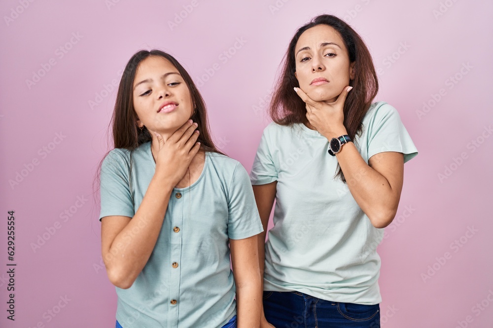 Young mother and daughter standing over pink background touching painful neck, sore throat for flu, clod and infection Young mother and daughter standing over pink background touching painful neck, sore throat for flu, clod and infection