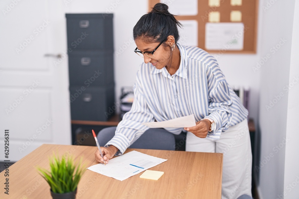 Young beautiful hispanic woman business worker reading document writing on notebook at office Young beautiful hispanic woman business worker reading document writing on notebook at office