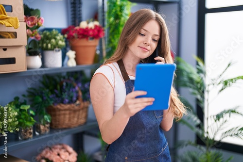 Young woman florist talking on smartphone using touchpad at florist shop